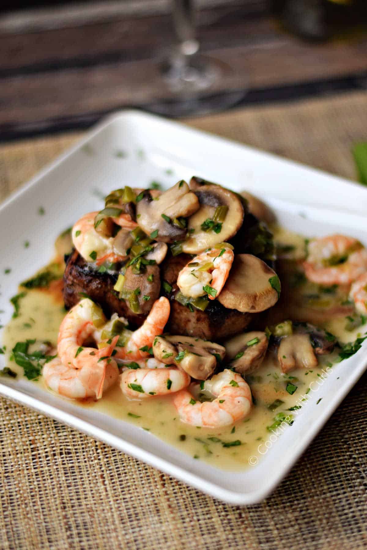 Beef tenderloin topped with a shrimp and mushroom sauce on a square serving plate.