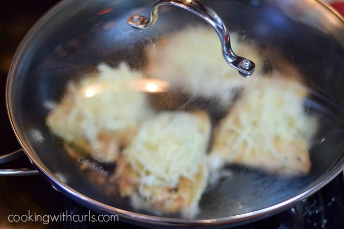 Cheese topped chicken breasts in a covered skillet.