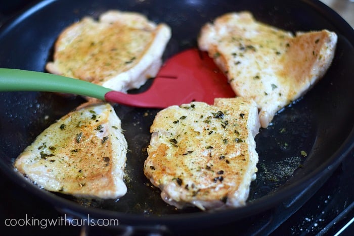 Four browned chicken breasts in a skillet.