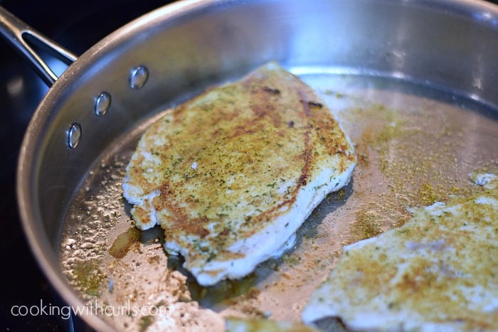 Two cooked, seasoned chicken breasts in a skillet.