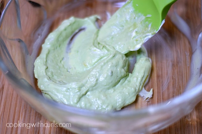 Lime juice, yogurt, garlic, salt, and pepper mixed with avocado in a large mixing bowl.