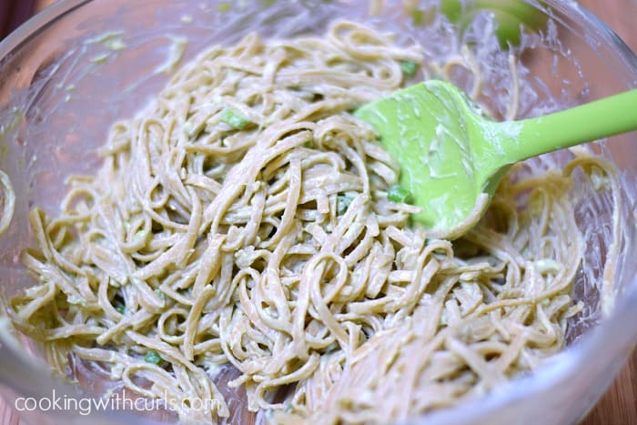 Cooked pasta noodles stirred into the guacamole mixture in a large bowl.
