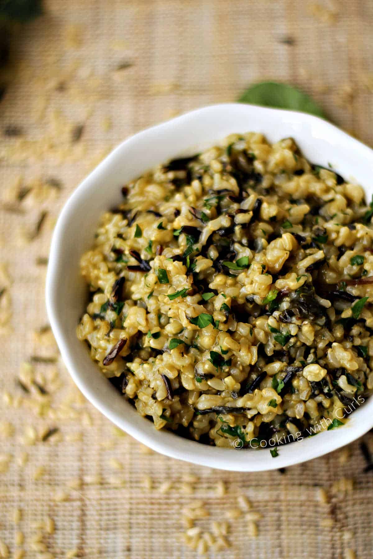 A serving bowl filled with savory wild and brown rice pilaf with fresh chopped parsley on top.
