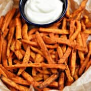 A parchment lined basket of sweet potato fries with aioli in a small bowl.