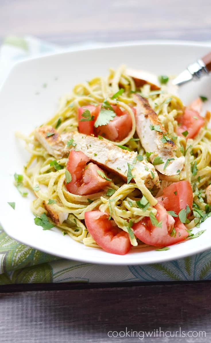 Guacamole linguini topped with sliced chicken breast, tomato, and parsley in a serving bowl.