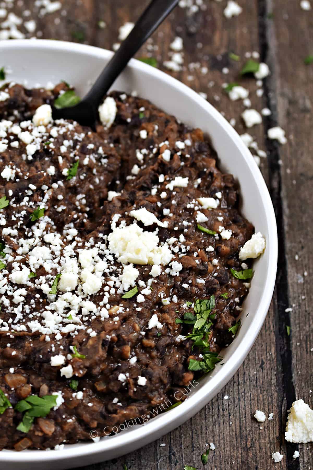 A bowl of Black Refried Beans topped with crumbled queso and cilantro. 