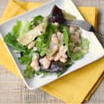 Artichoke and White Bean Salad on a square white plate sitting on a bright yellow napkin