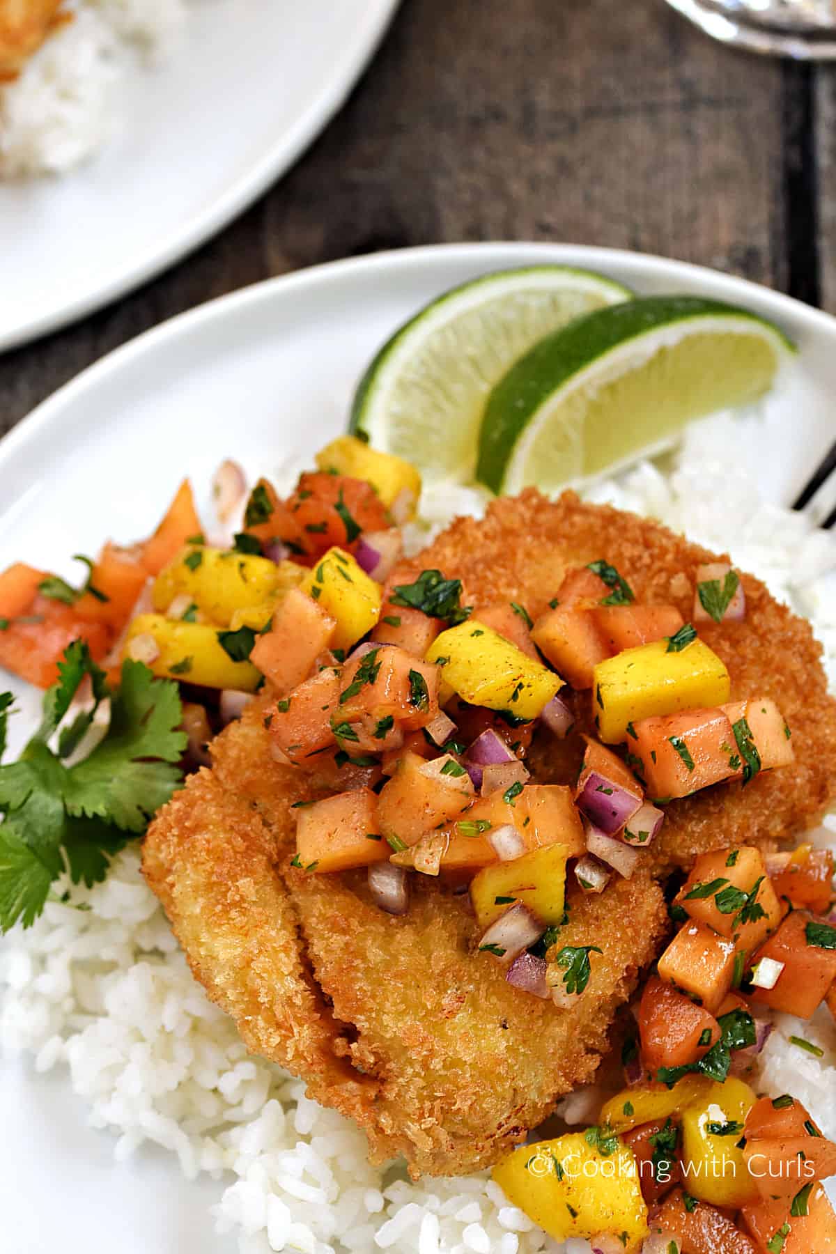 Crispy fried panko crusted mahi mahi on a bed or white rice topped with papaya mango salsa with two lime wedges for garnish. 