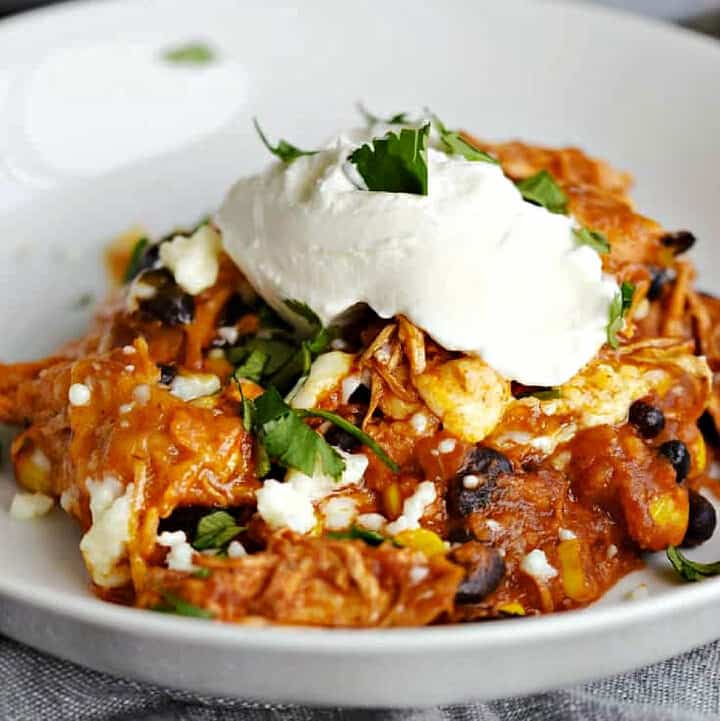 A Mexican casserole with tortillas, tomatoes, corn, and black beans topped with sour cream and black olives.