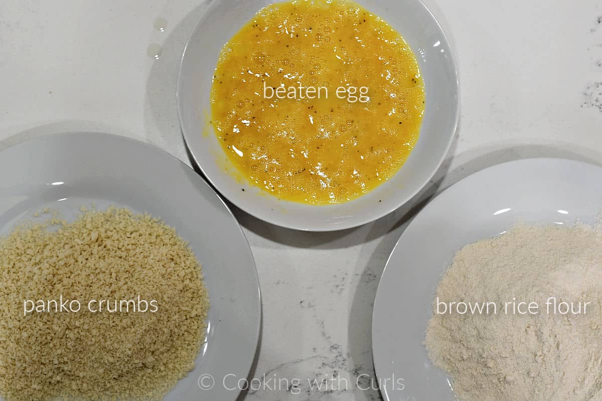 Panko crumbs on a large plate, beaten eggs in a bowl, brown rice flour on a large plate.