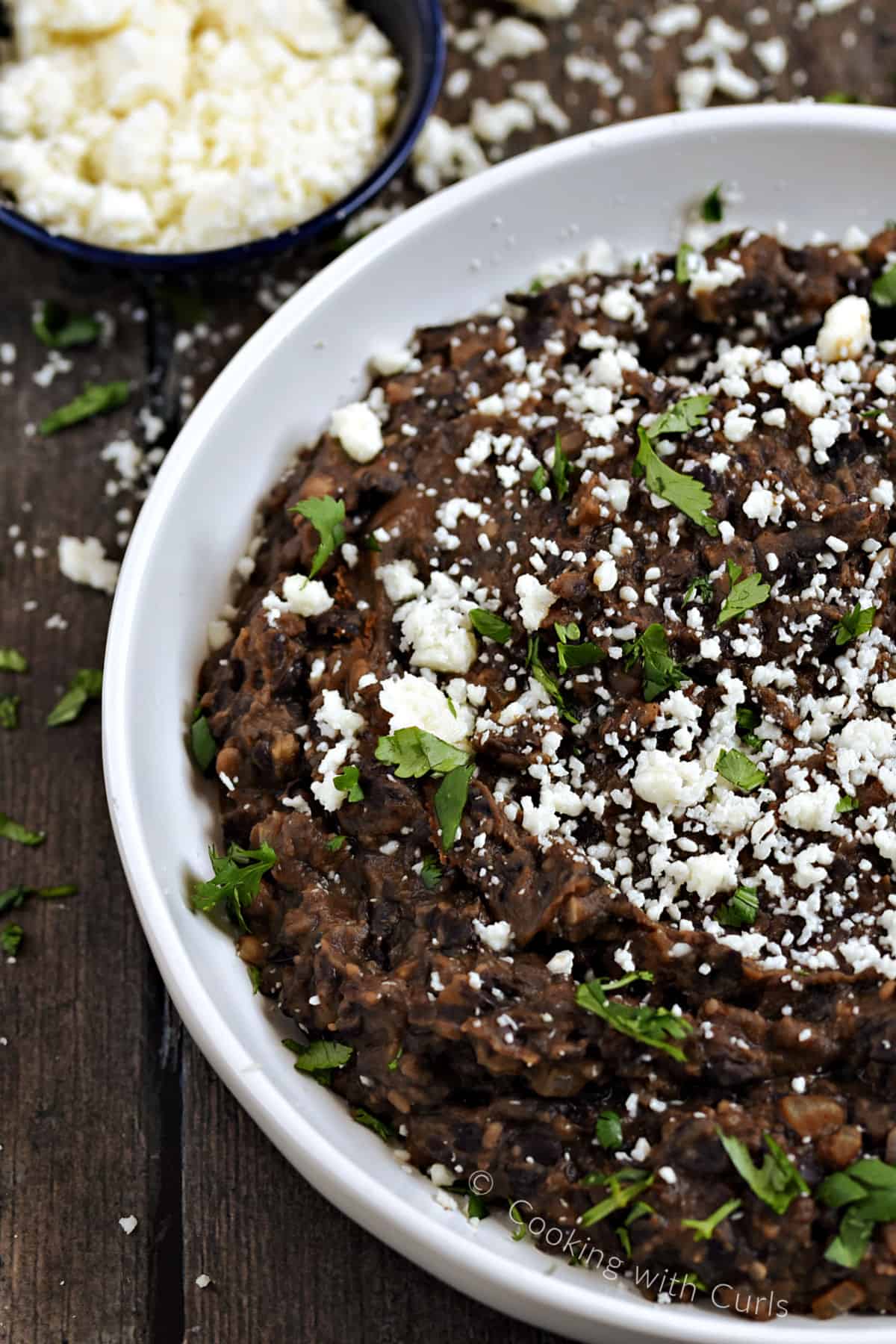 Refried Black Beans in a serving bowl topped with crumbled cheese and cilantro. 