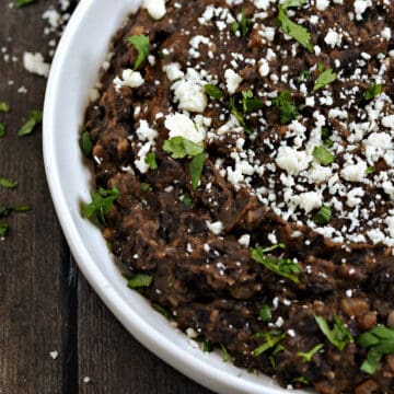 Refried Black Beans in a serving bowl topped with crumbled cheese and cilantro.