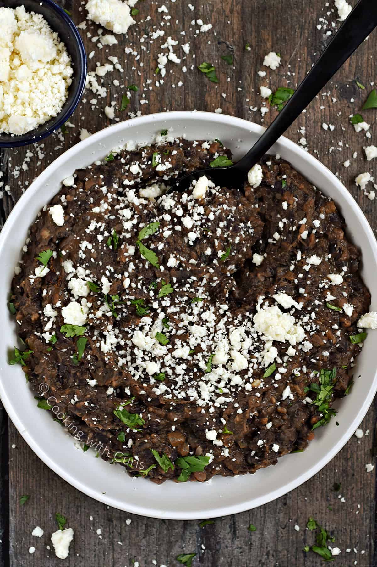 Looking down on a bowl of Refried Black Beans topped with crumbled queso and chopped cilantro. 