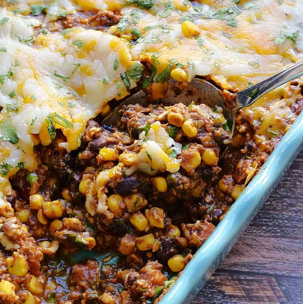 Dip made with black beans, corn, meat, and lots of melted cheese in a baking dish.