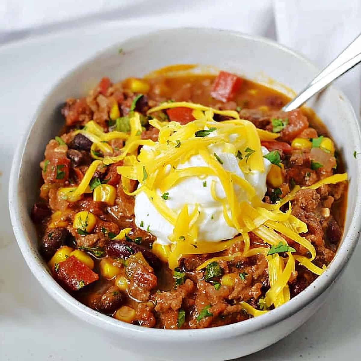 A bowl of chili made with black beans, corn, and tomatoes topped with sour cream and shredded cheddar cheese.