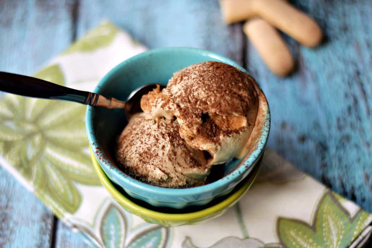 Two scoops of tiramisu ice cream dusted with cocoa powder in two stacked ice cream bowls.