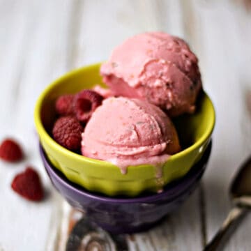 Two scoops of Raspberry Thyme Ice Cream in a green bowl bowl with fresh raspberries on the side.