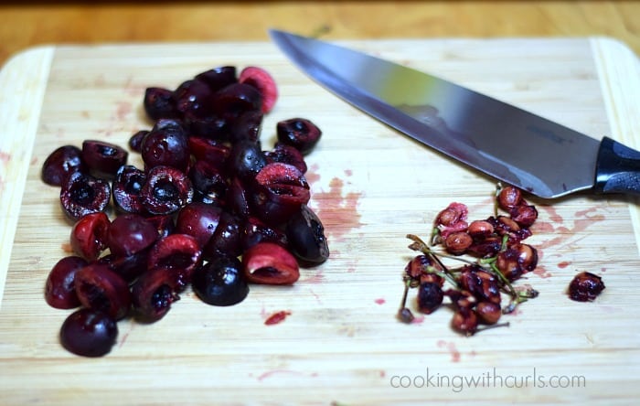 Pitted and halved cherries on a cutting board with a large knife.