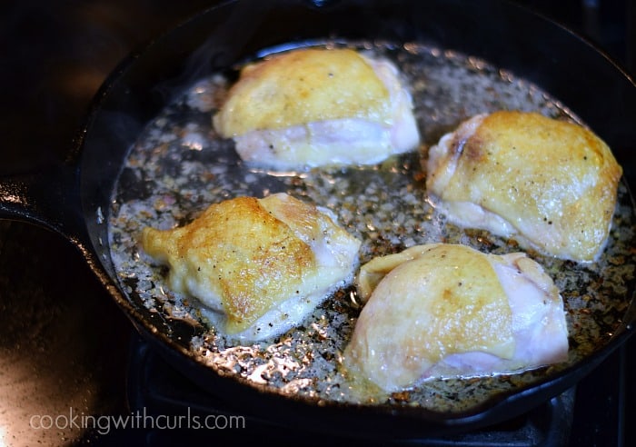 Four chicken thighs in a cast iron skillet with shallots and champagne.