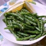 French Green Beans {Haricot Verts} in a white serving dish with lemon wedges on the side.