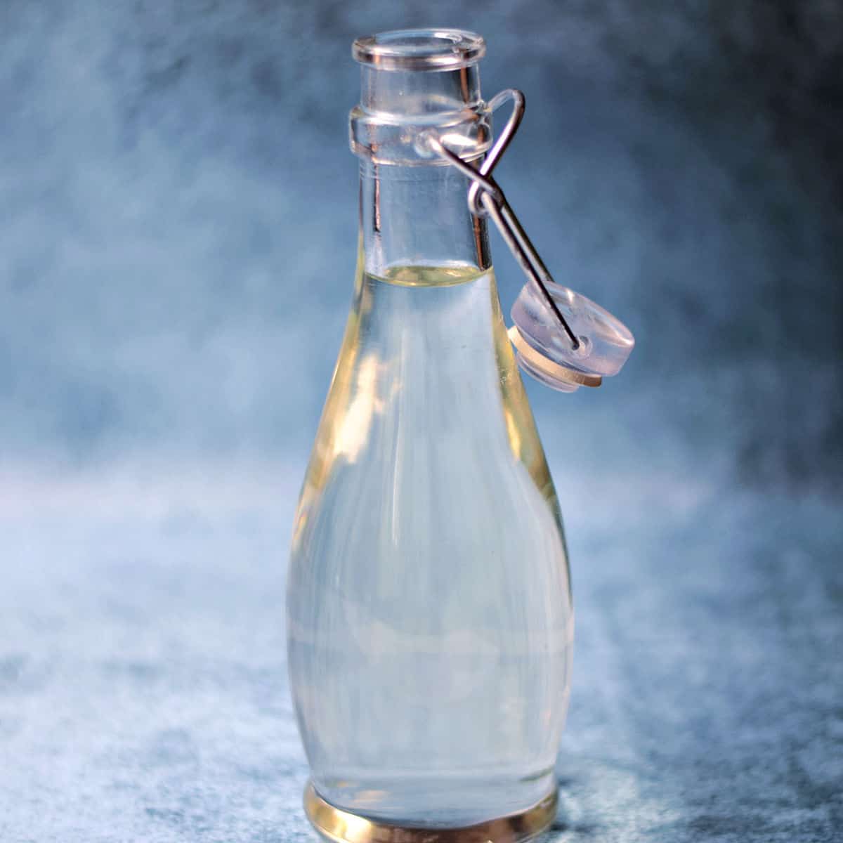 Clear simple syrup in a glass bottle with a blue sponged background.