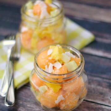 two tropical cantaloupe salads in glass jars with a green checkered napkin and two forks in the background
