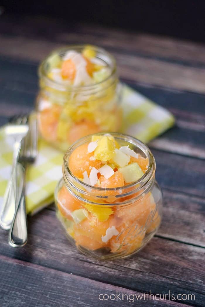 two tropical cantaloupe salads in glass jars with a green checkered napkin and two forks in the background