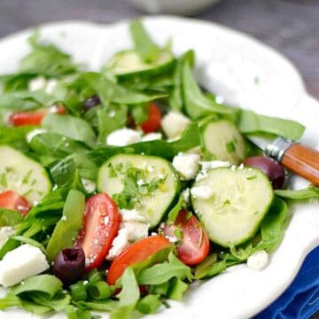 A fresh Greek Salad on a white plate sitting on a bright blue napkin