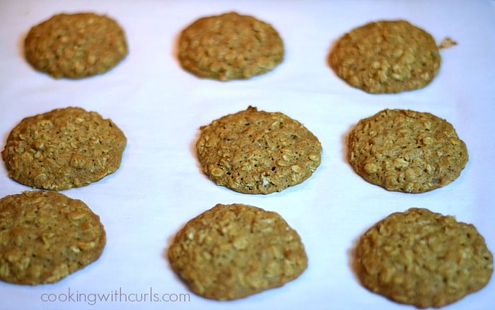 Nine baked oatmeal cookies on a parchment paper lined baking sheet.