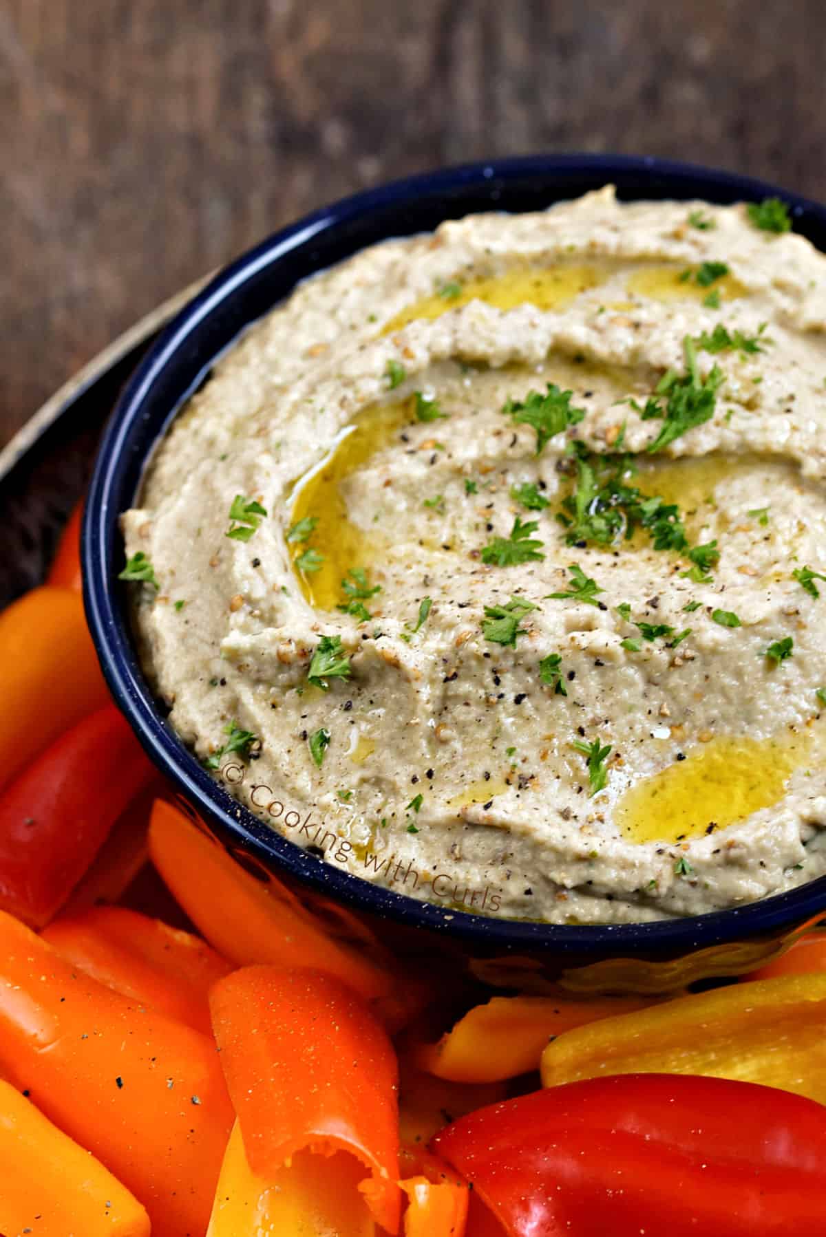 A bowl of Greek Eggplant Dip sitting on a platter filled with colorful sliced bell peppers.