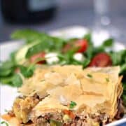 Greek Summery Meat Pie on a white plate with a Greek salad on the side and title graphic across the top.