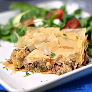 Greek Summery Meat Pie on a white plate with a Greek salad on the side