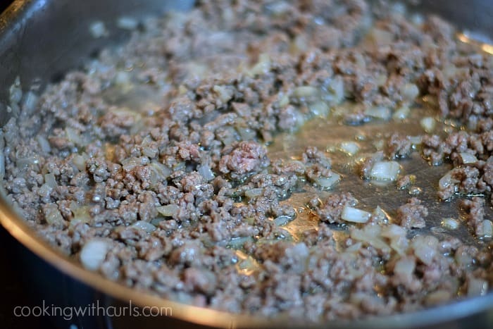 Ground meat and diced onions cooking in a large skillet.