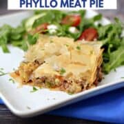 A slice of Greek Phyllo Meat Pie on a plate with a Greek lettuce salad on the side and title graphic across the top.