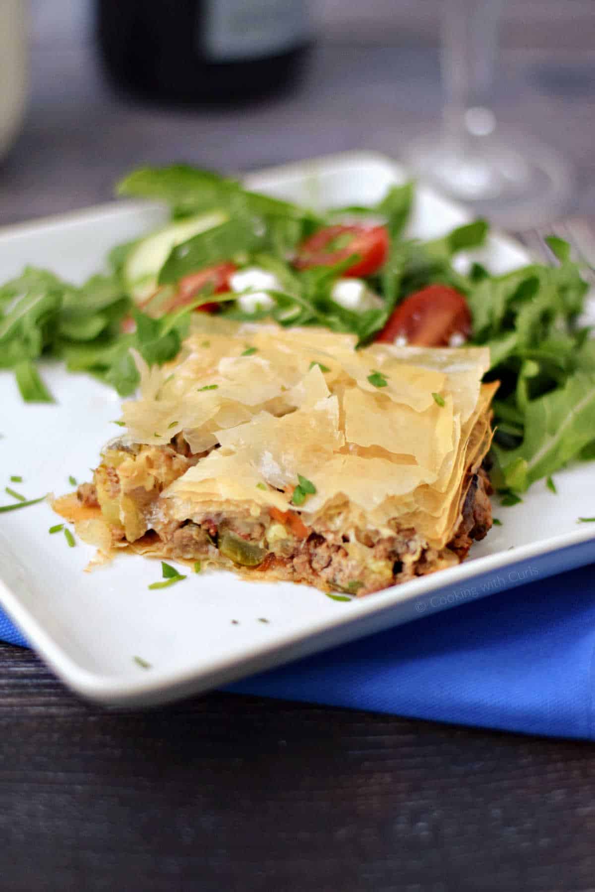 A slice of Greek Phyllo Meat Pie on a plate with a Greek lettuce salad on the side.