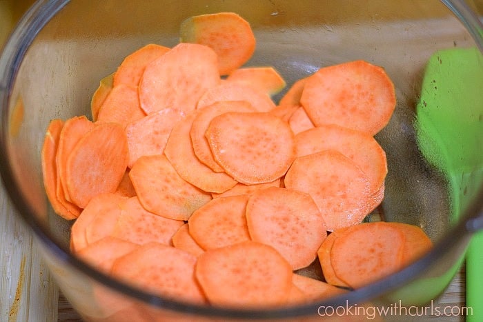Sweet potato slices tossed with oil in a glass mixing bowl