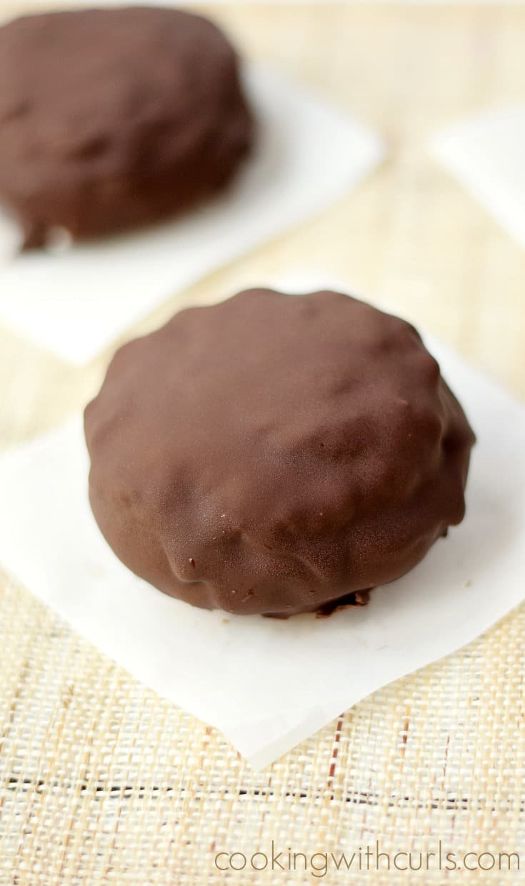 Two chocolate coated ice cream sandwiches sitting on parchment paper squares.