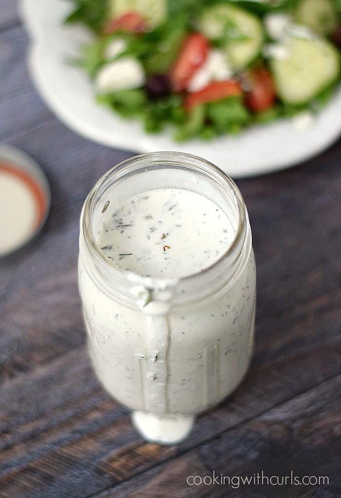Creamy feta dressing in a mason jar with a Greek salad in the background.