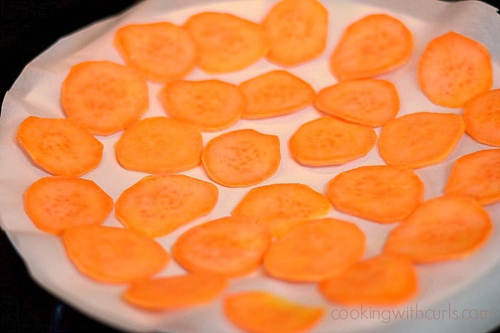 Thinly sliced sweet potato slices on a parchment lined plate