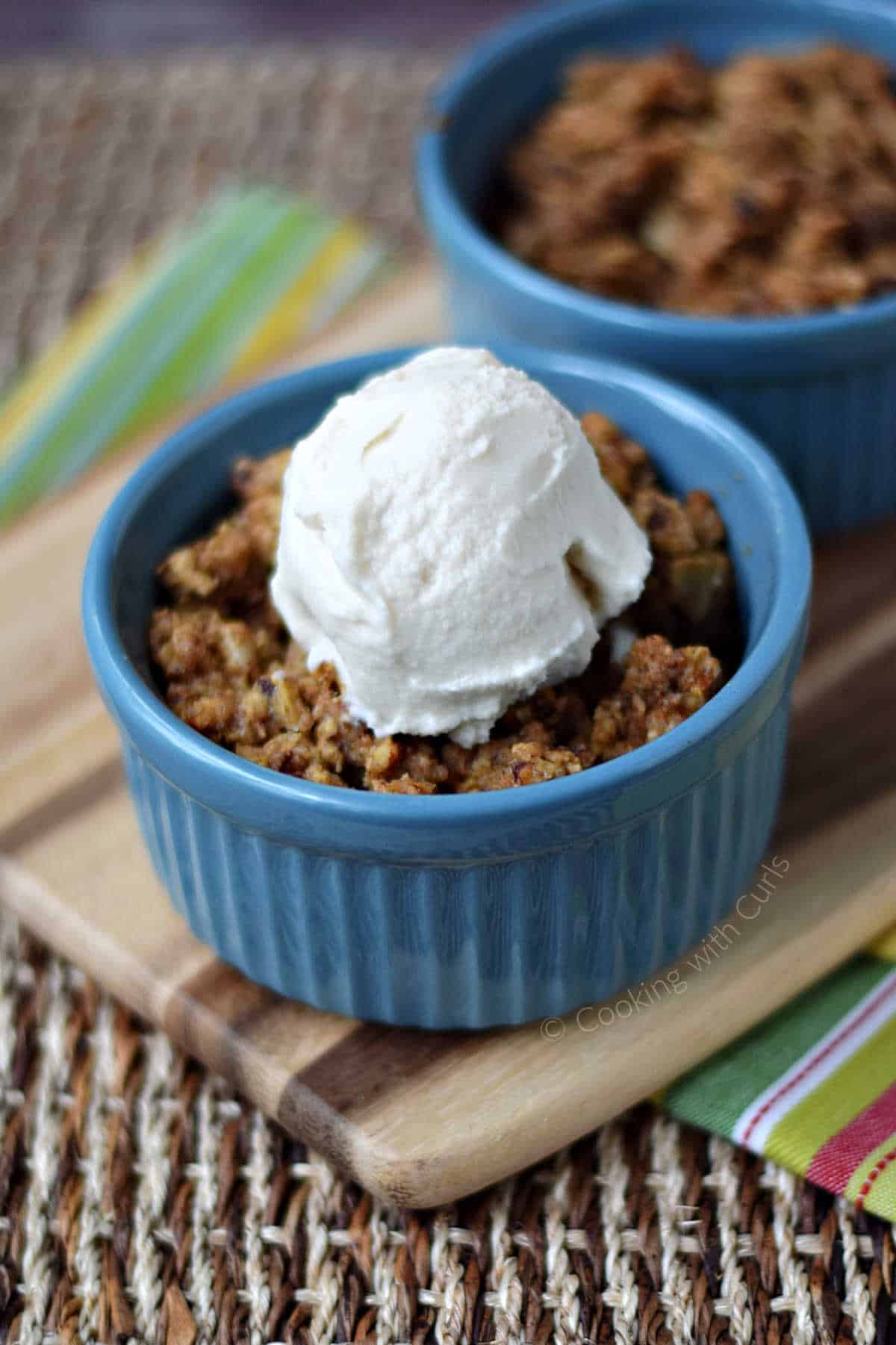 Two ramekins of rhubarb crisp topped with a scoop of vanilla ice cream.