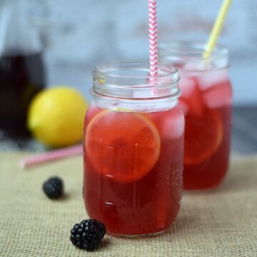 Blackberry Passion Tea Lemonade in glass mason jars with colorful paper straws and a lemon in the background