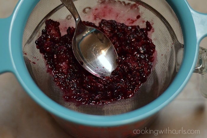 A spoon smashing the blackberries in a strainer.