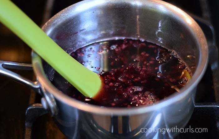 A green potato masher smashing the berries in a saucepan.