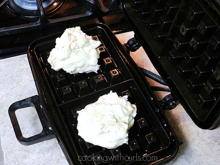 A scoop of waffle batter in the center of two separate side of a Belgian waffle maker.