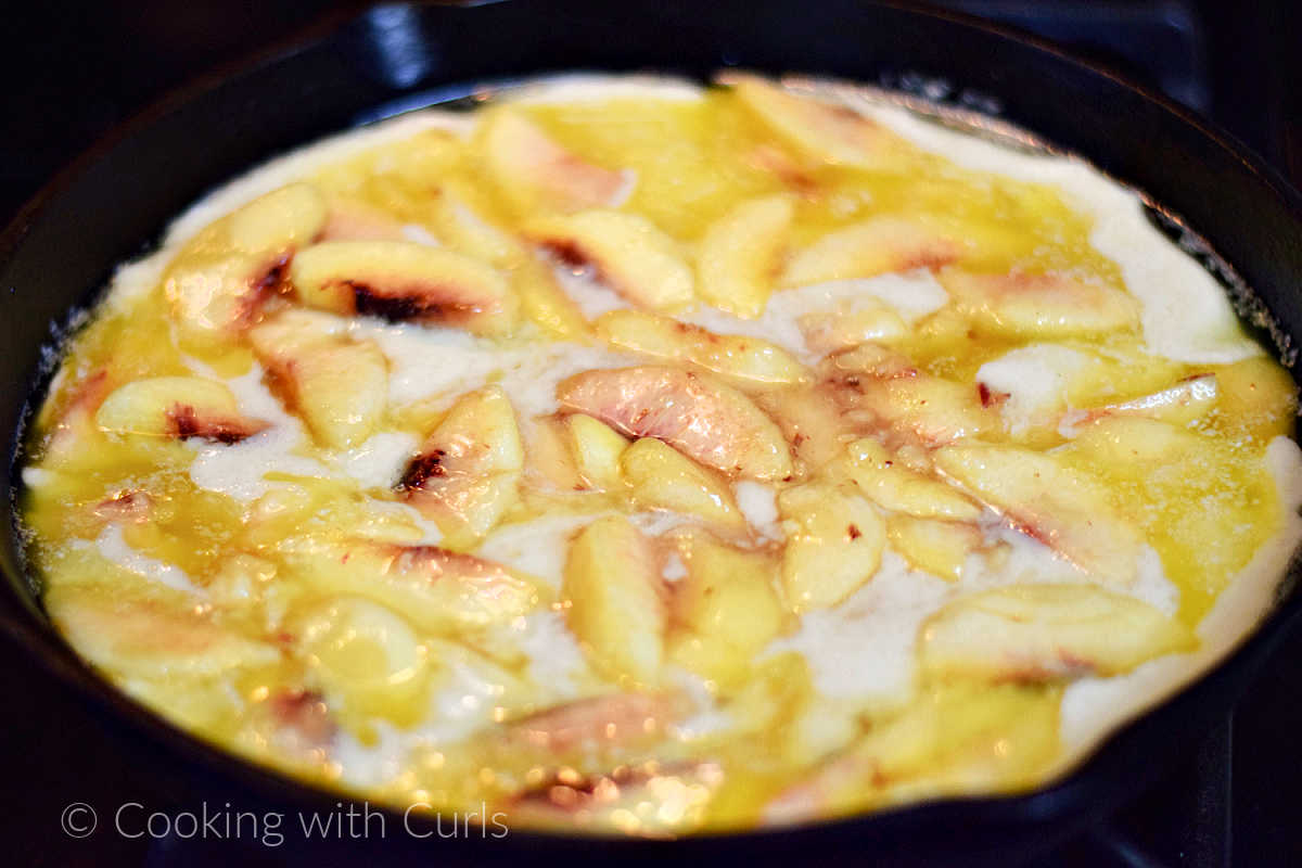 Peach slices spread over the batter in cast iron skillet.
