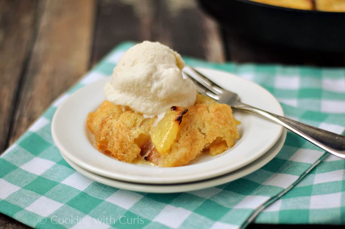 Peach cobbler on a plate topped with vanilla ice cream on a small plate.