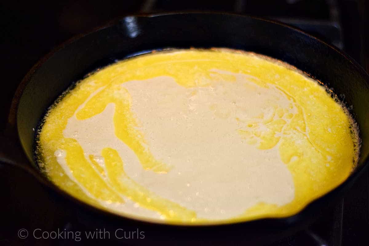 Peach cobbler batter poured into the melted butter in cast iron skillet.