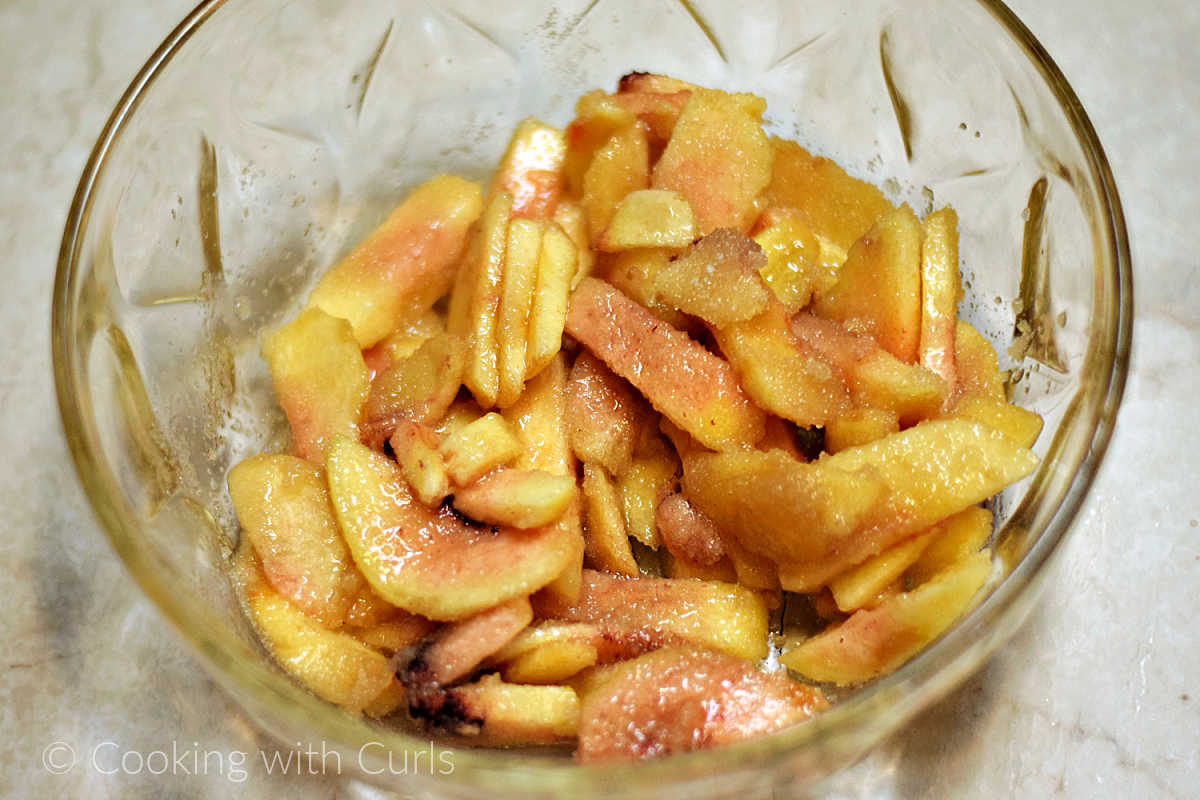 Sliced peaches mixed with sugar in a mixing bowl.
