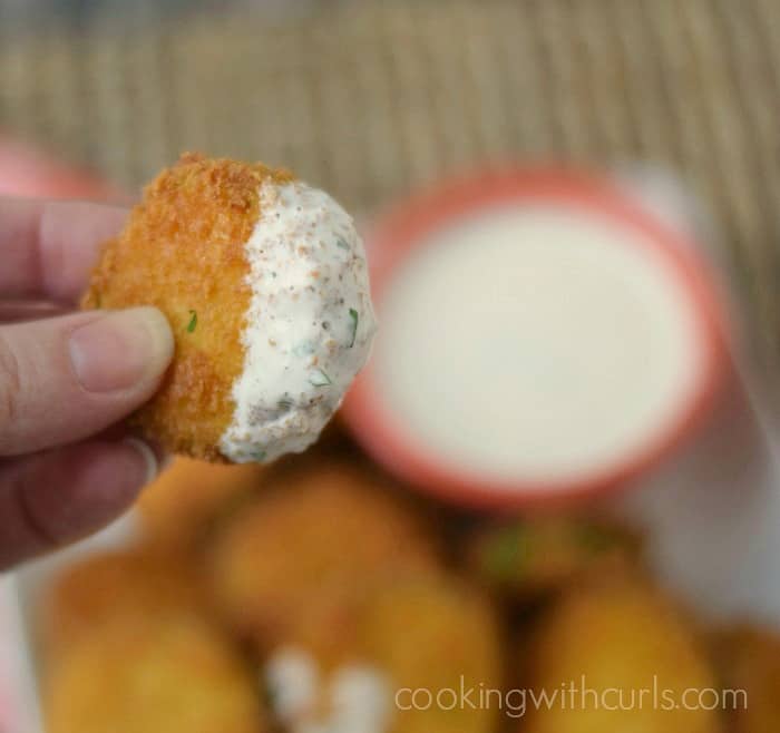 A woman's hand holding fried zucchini that has been dipped in ranch dressing.