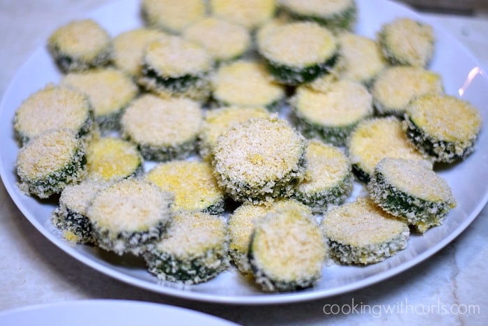 A plate full of coated zucchini slices ready to be fried.